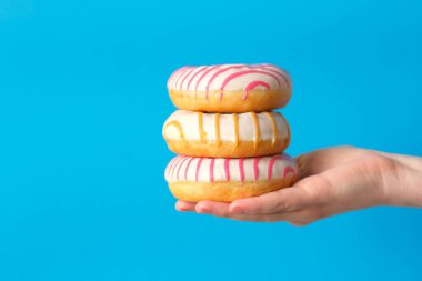 Kadın, mavi arka planda donutları tutuyor.