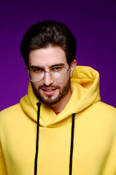Un giovane di 25-30 anni in occhiali e una felpa gialla posa emotivamente su uno sfondo viola. — Foto Stock
