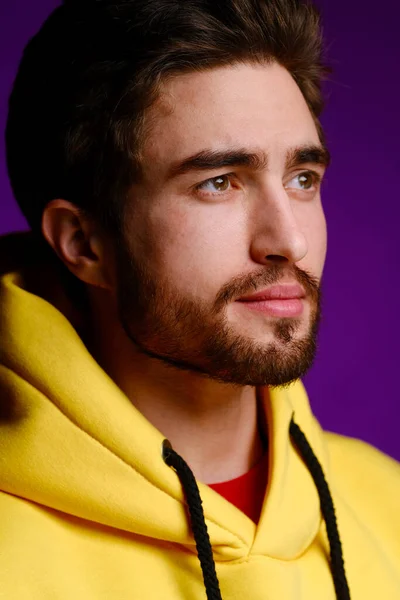 Mladý muž 25-30 let ve žluté mikině emocionálně pózuje na purpurovém pozadí. — Stock fotografie