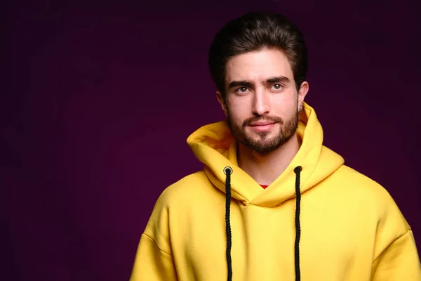 A young man of 25-30 years in yellow sweatshirt emotionally poses on a purple background. — Stock Photo, Image