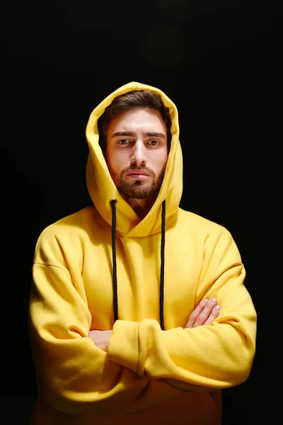 Un jeune homme de 25 à 30 ans en sweat-shirt jaune se dresse contre un mur noir. — Photo