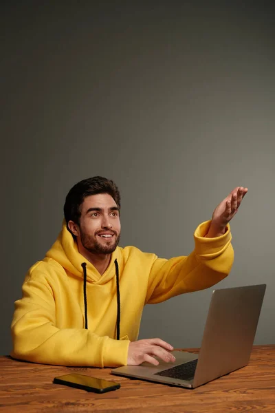 Un joven con diferentes emociones en una sudadera amarilla funciona con un ordenador portátil y un teléfono inteligente . — Foto de Stock