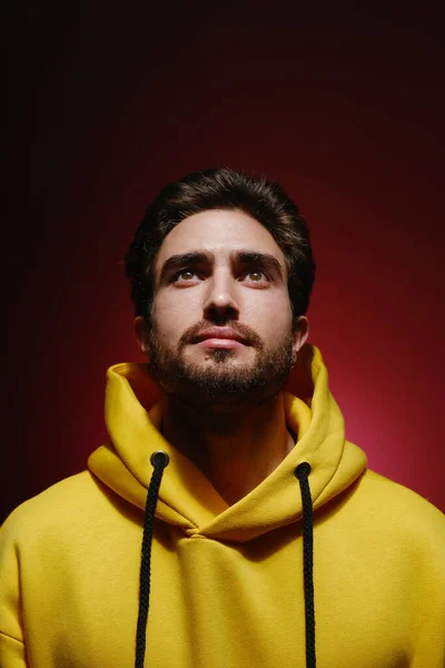 Portrait d'un jeune homme de 25 à 30 ans levant les yeux dans un sweat-shirt jaune sur fond de mur rouge. — Photo