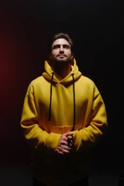 25-30 yaşlarında bir gencin portresi kırmızı arka planda sarı bir kazakla yukarı bakıyor.. 