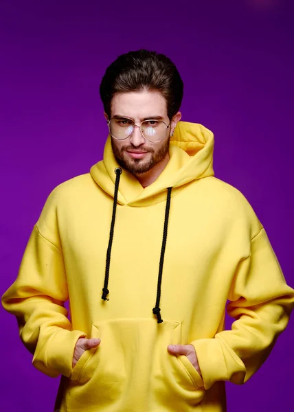 Un jeune homme de 25-30 ans en lunettes et un sweat-shirt jaune pose émotionnellement sur un fond violet. — Photo