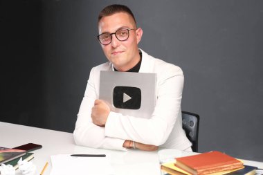 Kısa saçlı, gözlüklü, açık tişörtlü, elinde oyun sembolü olan 30-35 yaşlarında bir adam..