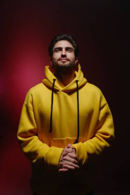 25-30 yaşlarında bir gencin portresi kırmızı arka planda sarı bir kazakla yukarı bakıyor.. 