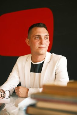 Genç bir öğretmen beyaz ceketli ve gözlüklü bir adam öğrencilerinin ödevlerini kontrol ediyor ve yeni bir derse hazırlanıyor.