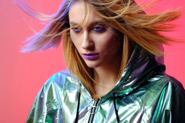 Parlak makyajlı güzel bir kız metalik bir rüzgarlıkla moda pembe neon arka planda poz veriyor..