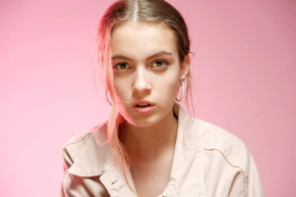 Uma menina em uma ganga rosa mostra emoções diferentes e posa em um fundo rosa . — Fotografia de Stock