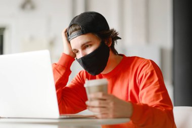 Adam açık alanda bir masada tek başına oturuyor, kahve içiyor ve dizüstü bilgisayarı üzerinde çalışıyor. Serbest konsept