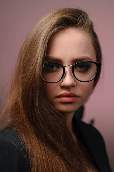 A young girl 20-25 years old in glasses, a jacket in the image of a teacher posing on a pink background. — Stock Photo, Image