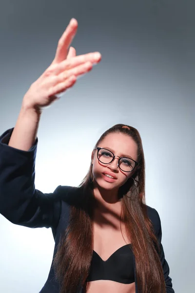 Una joven de 20-25 años de edad en gafas, una chaqueta y con una cola en la imagen de un profesor posa sobre un fondo gris y muestra diferentes emociones — Foto de Stock