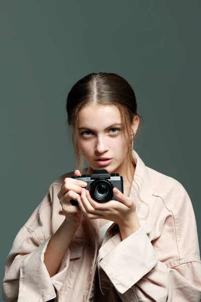 A girl photographer in a pink jacket holds a mirrorless camera in her hands.