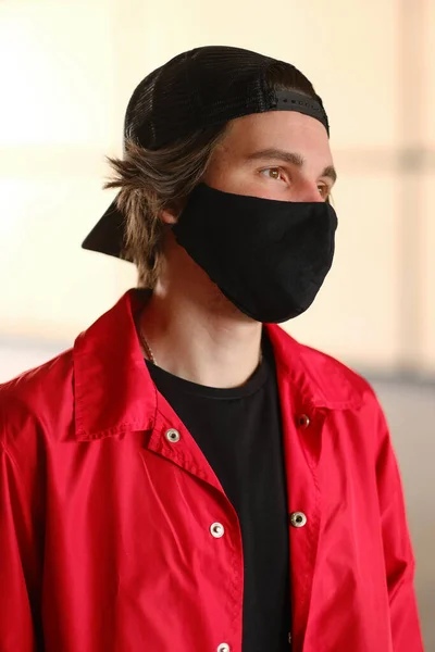 Портрет молодого человека 25-30 лет в черной защитной маске, черной кепке и красной куртке. — стоковое фото