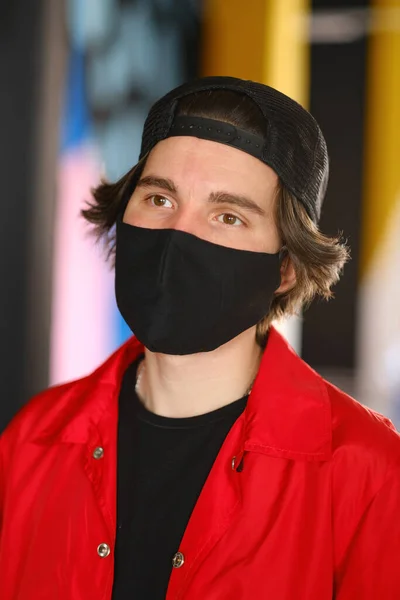 Retrato de un joven de 25-30 años con máscara protectora negra, gorra negra y chaqueta roja . — Foto de Stock