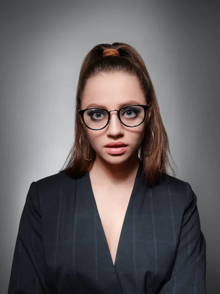 Une jeune fille de 20-25 ans dans des lunettes, une veste et avec une queue à l'image d'un professeur pose sur un fond gris et montre différentes émotions — Photo