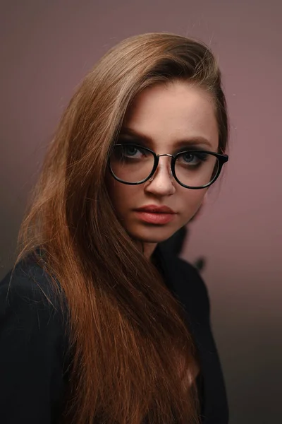 Una joven de 20-25 años de edad en gafas, una chaqueta en la imagen de un profesor posando sobre un fondo rosa . —  Fotos de Stock