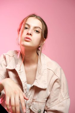 Pembe kot giyen bir kız farklı duygular gösterir ve pembe arka planda poz verir..