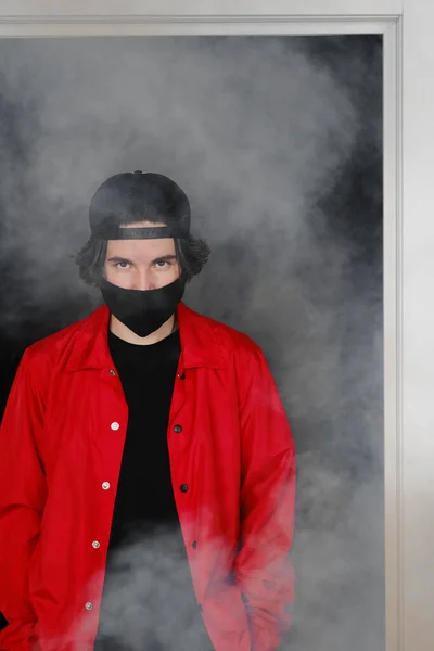 Portrait d'un jeune homme de 25 à 30 ans portant un masque de protection noir, une casquette et une veste rouge. — Photo