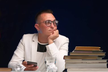 Genç bir öğretmen beyaz ceketli ve gözlüklü bir adam öğrencilerinin ödevlerini kontrol ediyor ve yeni bir derse hazırlanıyor.