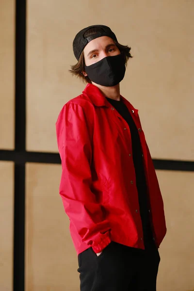 Retrato de un joven de 25-30 años con máscara protectora negra, gorra negra y chaqueta roja . — Foto de Stock