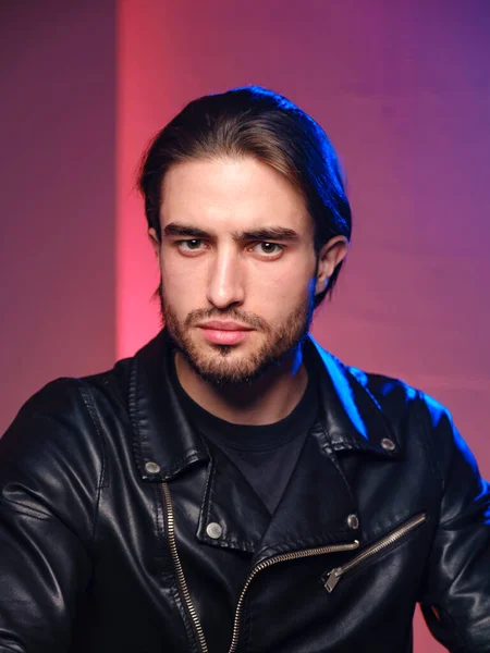 Un jeune homme de 25-30 ans dans une veste en cuir pose émotionnellement sur un fond violet. — Photo