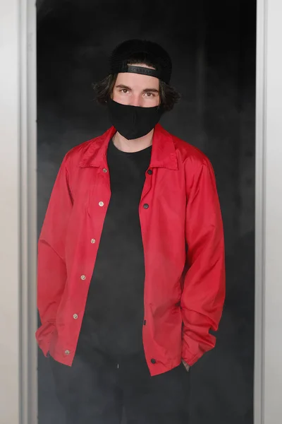 Porträt eines jungen Mannes von 25-30 Jahren mit schwarzer Schutzmaske, Mütze und roter Jacke. — Stockfoto