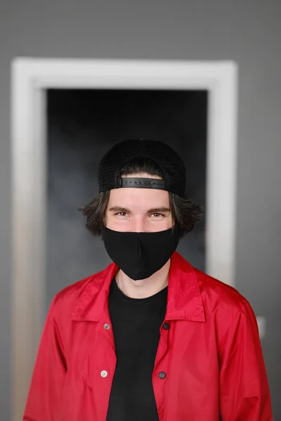 Retrato de un joven de 25-30 años con máscara protectora negra, gorra y chaqueta roja . — Foto de Stock