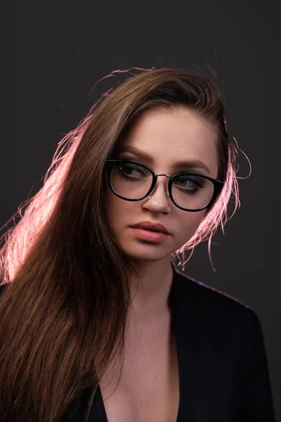 A young girl 20-25 years old in glasses, a jacket in the image of a teacher posing on a pink background. — Stock Photo, Image