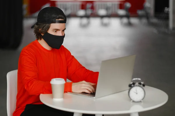 L'homme est assis seul à une table dans l'espace ouvert, buvant du café et travaillant sur son ordinateur portable. Concept freelance Images De Stock Libres De Droits