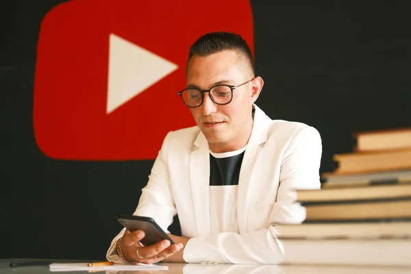 Un hombre de 30-35 años de edad, con un corte de pelo corto, con gafas, una camisa ligera, se sienta en una mesa y se le ocurre un guión para su vlog —  Fotos de Stock