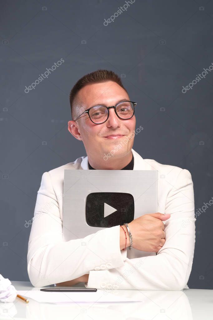A 30-35-year-old millennial man with a short haircut, glasses, in a light shirt, holds a sign with a play symbol in his hands. vlogging live feeds on social media network