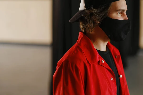 Retrato de un joven de 25-30 años con máscara protectora negra, gorra negra y chaqueta roja . Imagen De Stock