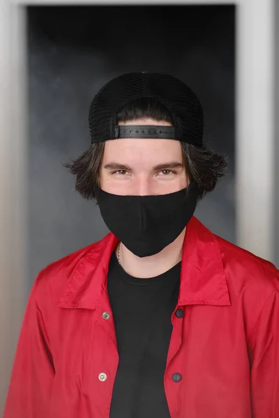 Portrait d'un jeune homme de 25 à 30 ans portant un masque de protection noir, une casquette et une veste rouge. Images De Stock Libres De Droits