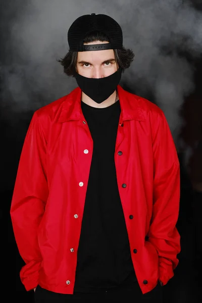 Portrait d'un jeune homme de 25 à 30 ans portant un masque de protection noir, une casquette et une veste rouge. — Photo