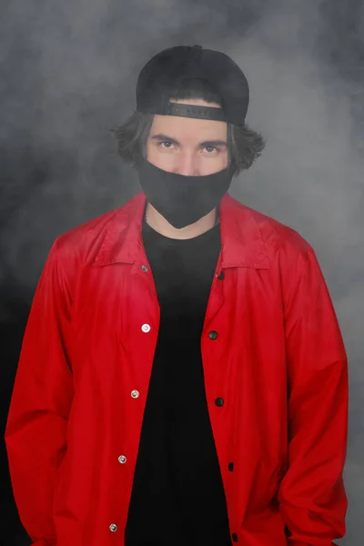 Retrato de un joven de 25-30 años con máscara protectora negra, gorra y chaqueta roja . — Foto de Stock