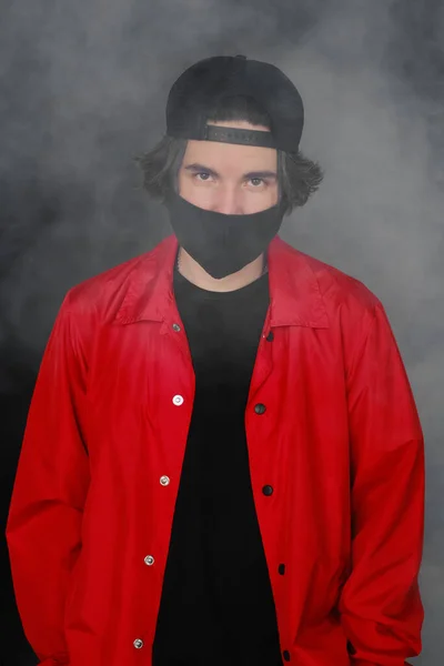 Retrato de un joven de 25-30 años con máscara protectora negra, gorra y chaqueta roja . Imagen De Stock