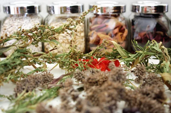 Bay leaves, dried cherry tomatoes, dried peppermint flowers, juniper berries, pepper peas and quinoa on white wooden background with fulled glass banks benind