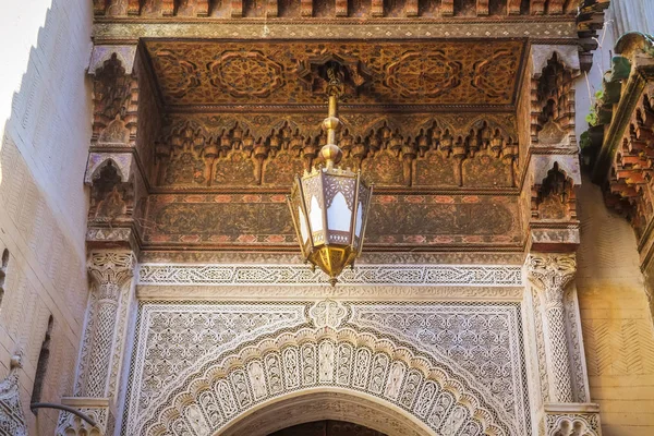 Beautiful ancient Moroccan art decoration in the city of Fez. Wooden carved ceiling, antique lamp and arabesque art on the wall. Fes el Bali, Morocco.