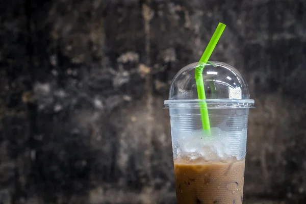 Plastic materials use, show transparent cup and green straw with partly consumed iced coffee inside.