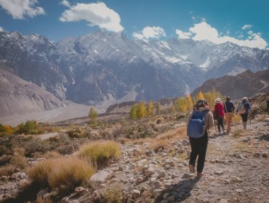 Tourists walking along the track in Passu trekking trail. Wildereness area surrounded by snow capped mountains in Karakoram range. Gilgit Baltistan, Pakistan. clipart