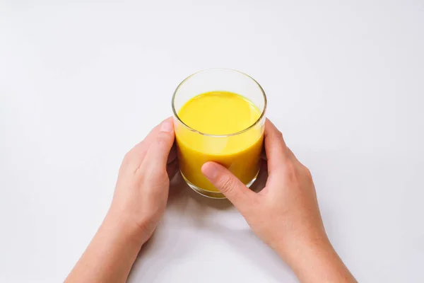 Beyaz masa zemininde, üzerinde fotokopi alanı olan sarı latte sütlü altın süt bardağı tutan eller.