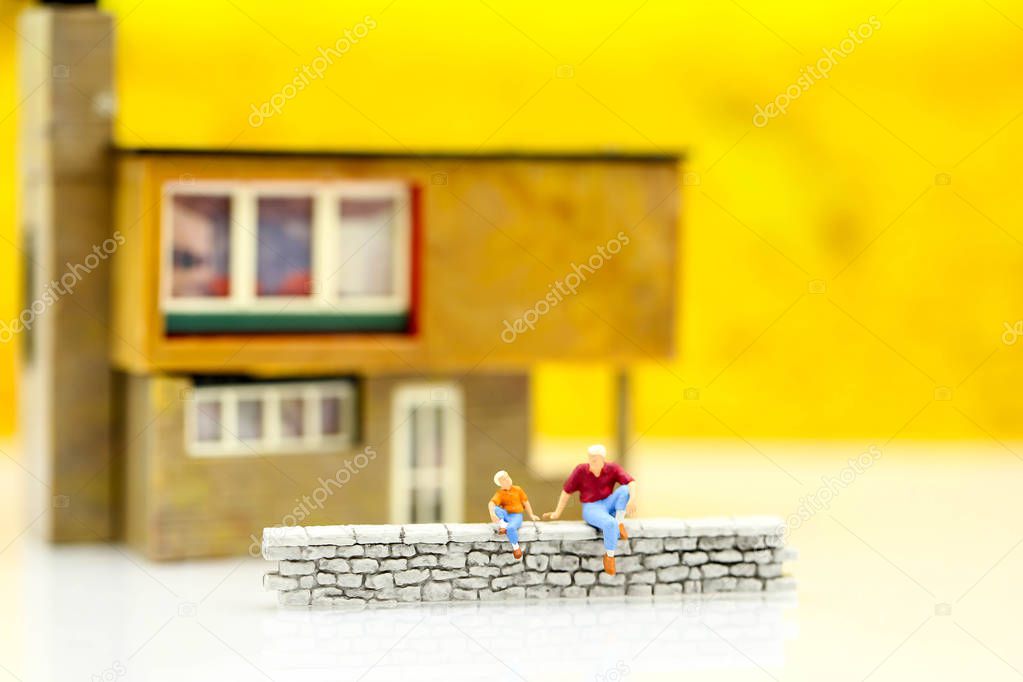 Miniature people : Family and children sitting of wall with house.