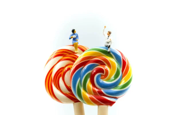 Minyatür insanlar: işadamı ve renkli şeker lolipop ile oturan arkadaş dinlenmek zaman kavramı.