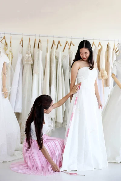 Beautiful bride getting dressed by her best friend in her wedding day and choosing a wedding dress in the shop and the shop assistant is helping her