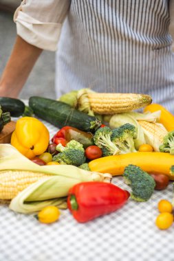 Yaz hasadı masada yatıyor. Bir sürü sebze: kabak, brokoli, domates, mısır, otlar, biber. Sebzelerin yattığı masanın yanında bir çiftçi kız duruyor. Yüksek kalite fotoğraf