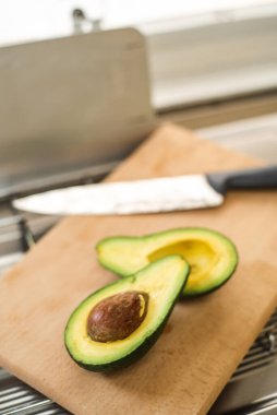 Avokado tahtada ikiye bölünmüş, yanında şef bıçağı, iki yeşil armut var..