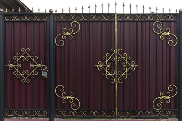 Süslü ve güzel ferforje çit kapısı kırmızı kahverengi ve altın boyalı. Doku olarak kullanılmak üzere doğal eski bir kapının fotoğrafı