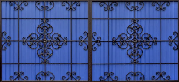 Ornate and beautiful wrought wide iron fence - gate painted scarlet blue and black. A photo of a natural old gate for use as a texture